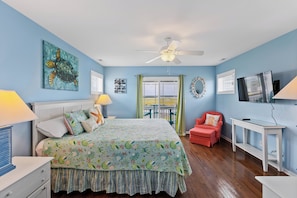 A bedroom with a bed, a ceiling fan, a TV, and a window with a view. - Palm Beach North by Topsail Realty (Sneads Ferry)