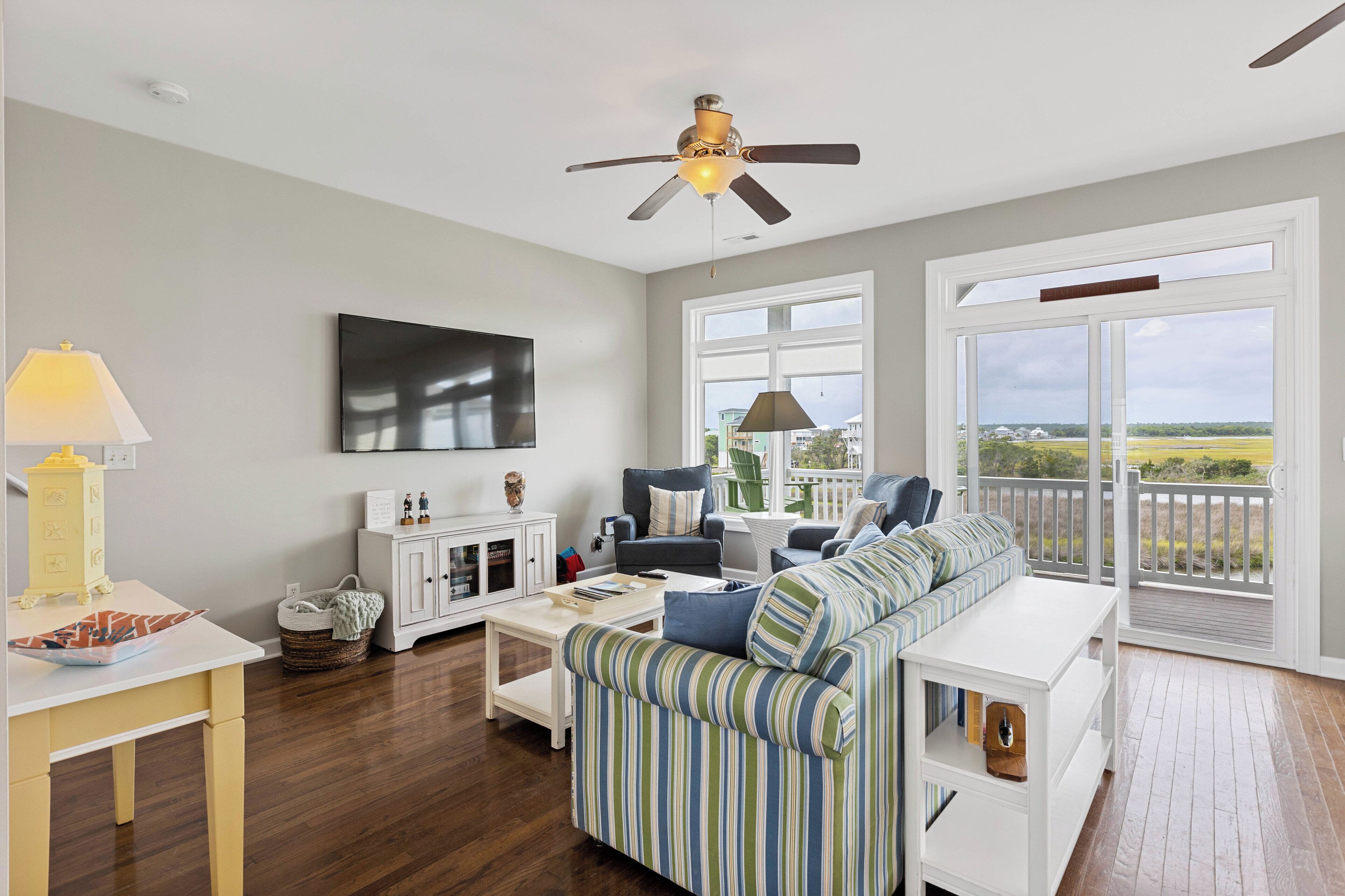A living room with a ceiling fan, a flat-screen TV, a sofa, a coffee table, and a view through large windows.
