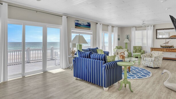 A spacious living room with a large sofa, a round table, and a view of the ocean through large sliding doors. - Topsail Escape by Topsail Realty (Sneads Ferry)