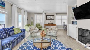 A living room with a blue-striped sofa, a glass coffee table, and a fireplace. - Topsail Escape by Topsail Realty (Sneads Ferry)
