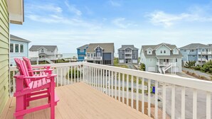A wooden deck with a pink Adirondack chair, overlooking a row of light blue and gray houses with a clear sky.