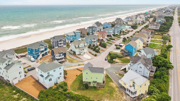 Un quartier résidentiel situé sur la côte, avec des maisons alignées le long de la plage, comprenant un mélange de bâtiments à un ou plusieurs étages, dont certains sont dotés de balcons apparents et d’allées.