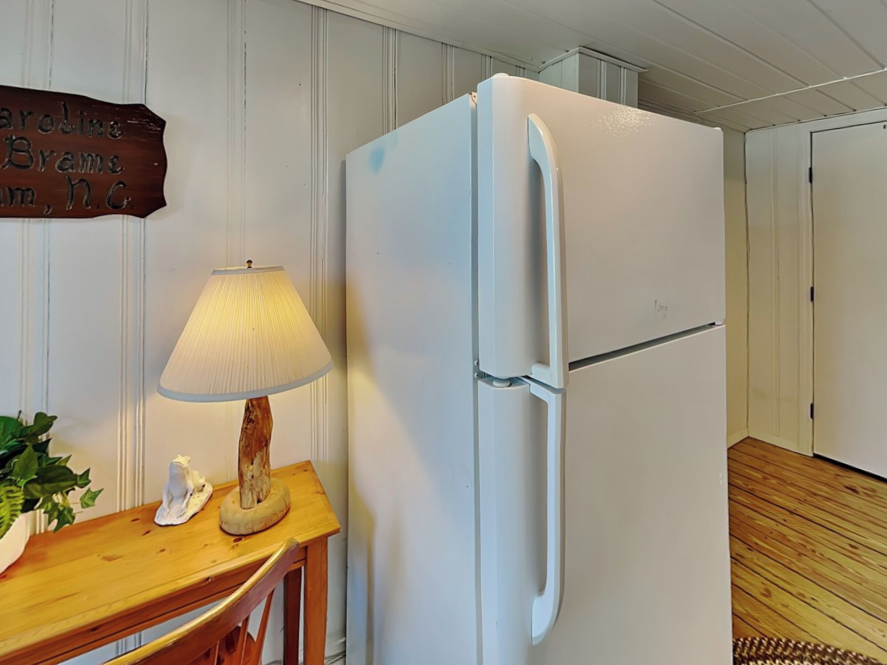 Una cocina con un refrigerador blanco, una mesa de madera con una lámpara y un letrero en la pared.