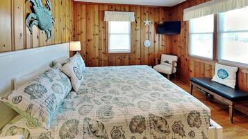 A bedroom with a bed, a chair, a television, and a window with blinds.