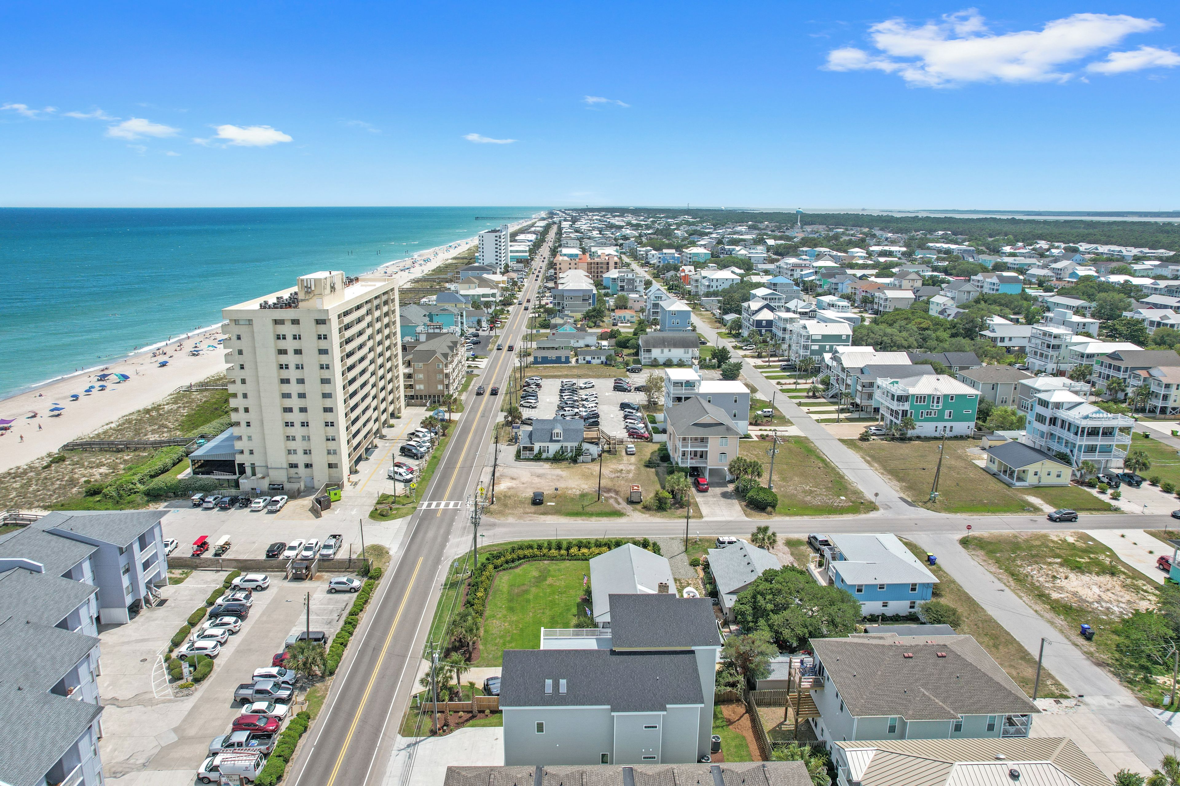 An aerial view of a coastal residential area with a beach, multi-story buildings, and a clear sky.