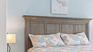 Un dormitorio con cabecera de madera, cama con ropa de cama estampada con motivos florales, mesita de noche con lámpara y una obra de arte colgada en la pared.