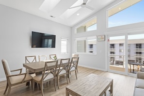 A modern dining area with a wooden table and chairs, a ceiling fan, and large windows offering a view of the outside. - Seadragon 1 by Carolina Retreats (Carolina Beach)