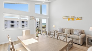 Ein modernes Wohnzimmer mit einem Holzesstisch, einem beigefarbenen Sofa und Meerblick durch große Fenster.