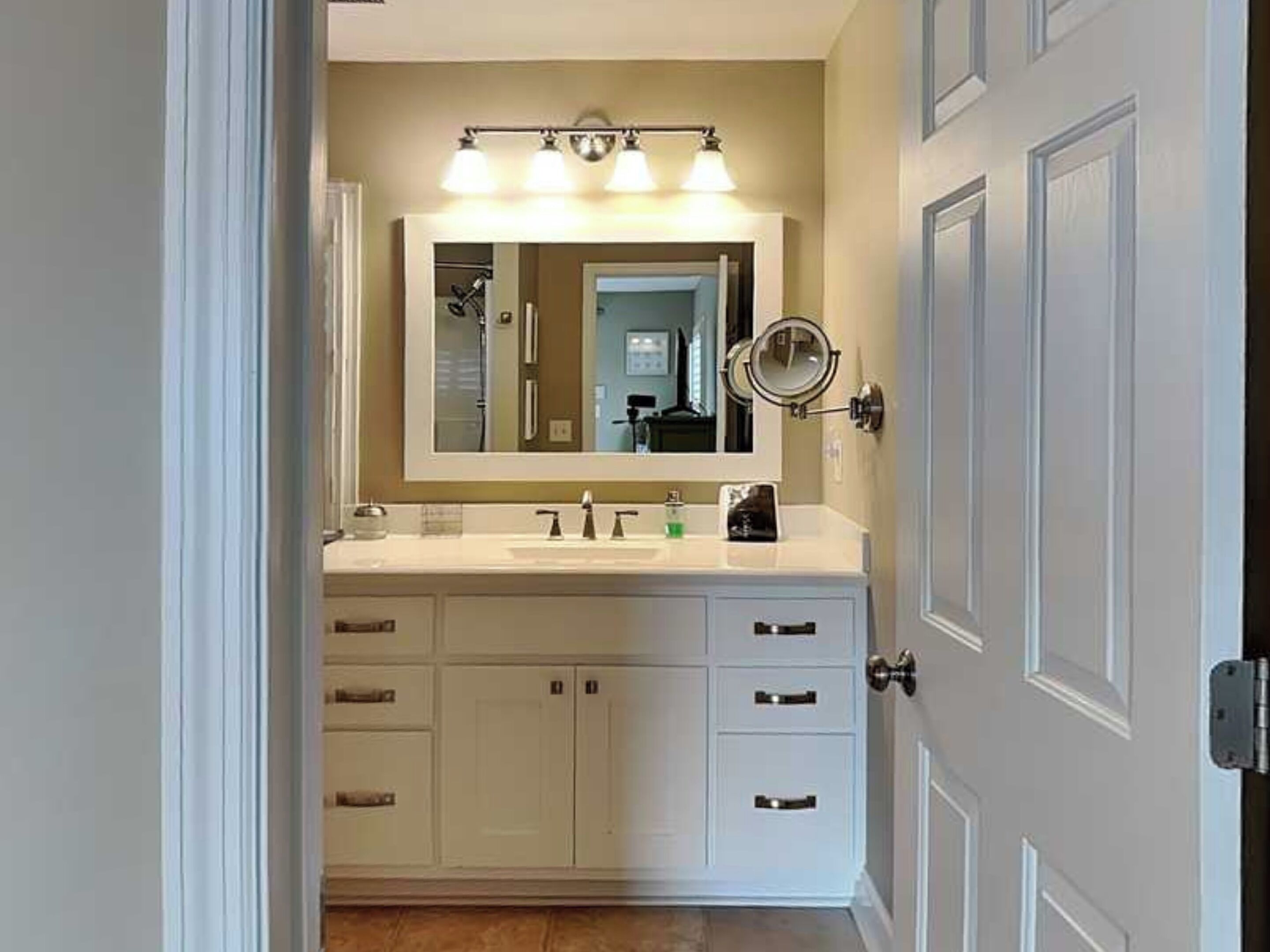 A bathroom with a white vanity, a large mirror, and a wall-mounted light fixture.