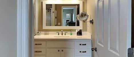 A bathroom with a white vanity, a large mirror, and a wall-mounted light fixture.
