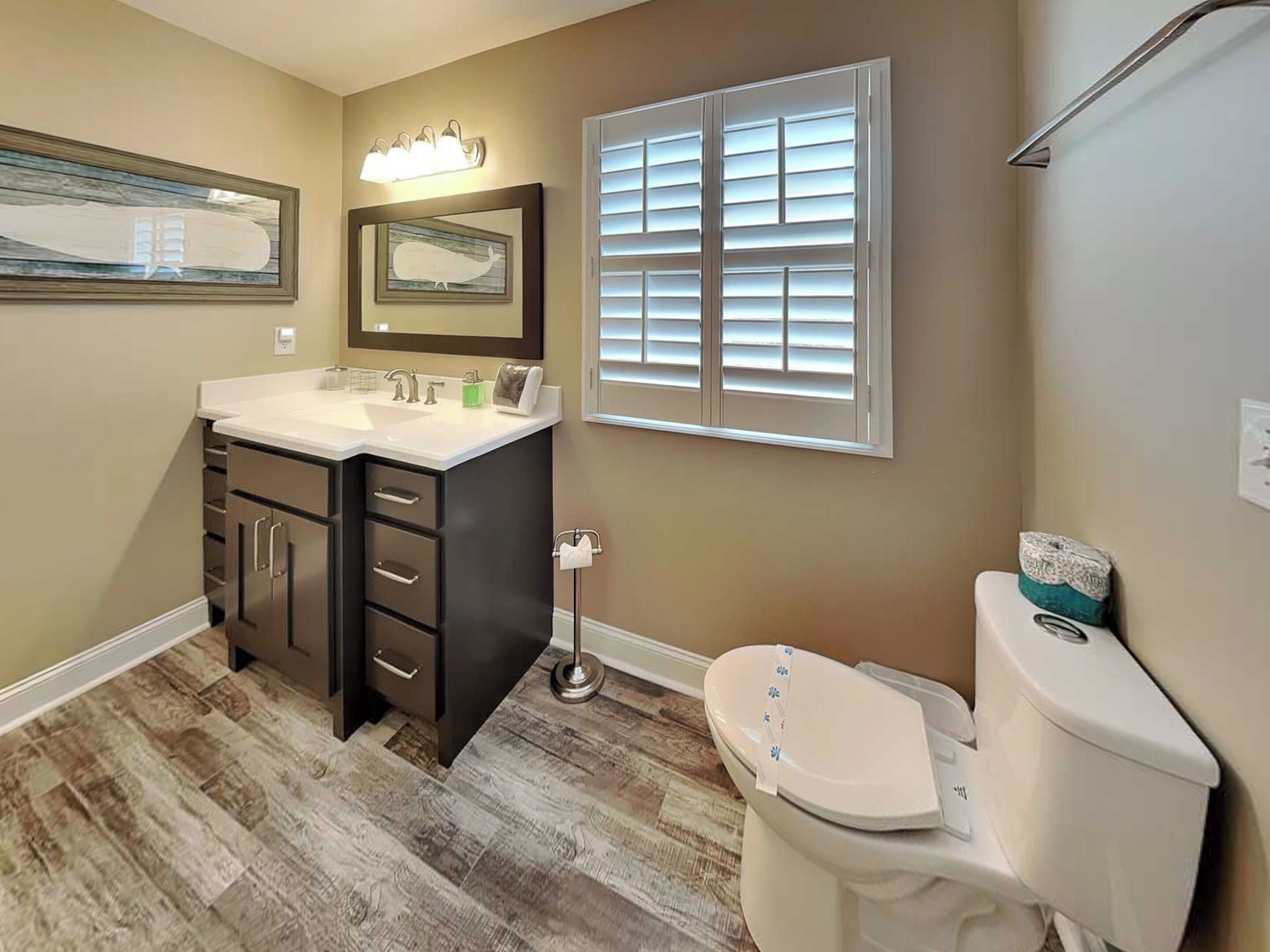 A bathroom with a vanity, toilet, and window with blinds.