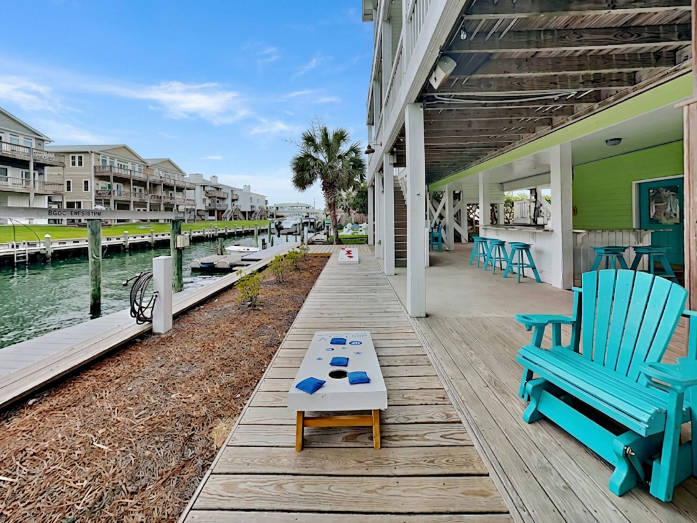 A wooden deck with a table and chairs, a marina with boats, and a building with a green exterior.