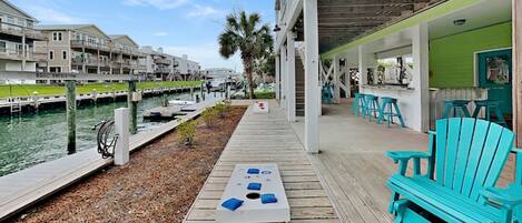 A wooden deck with a table and chairs, a marina with boats, and a building with a green exterior.