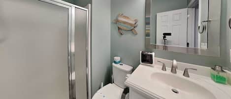 A bathroom with a shower, toilet, sink, and mirror.