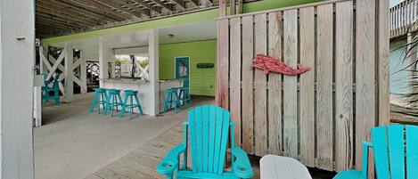A covered outdoor area with wooden flooring, turquoise Adirondack chairs, and a white Adirondack chair.