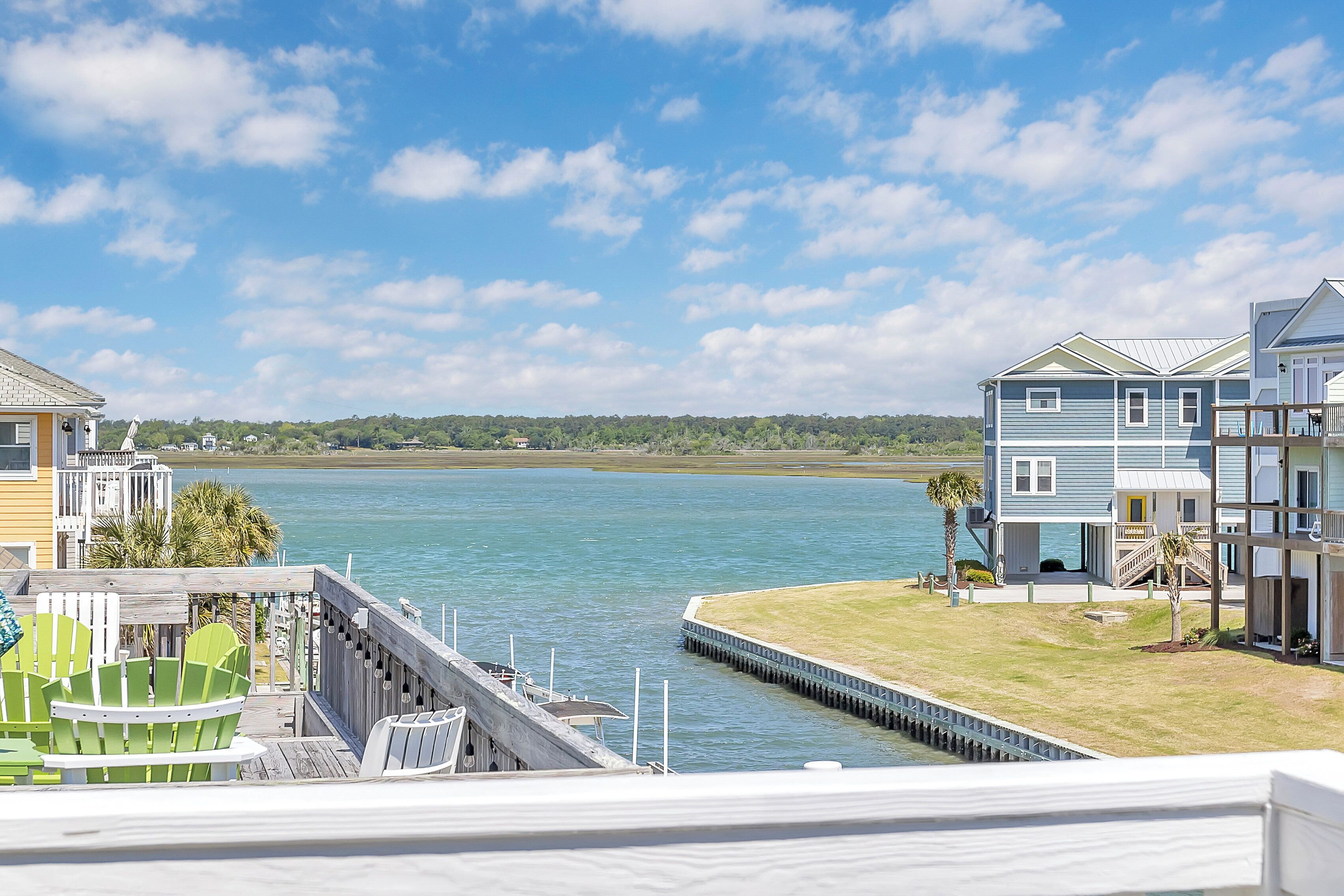 A waterfront property with a dock, green chairs, and a view of the water and distant trees.