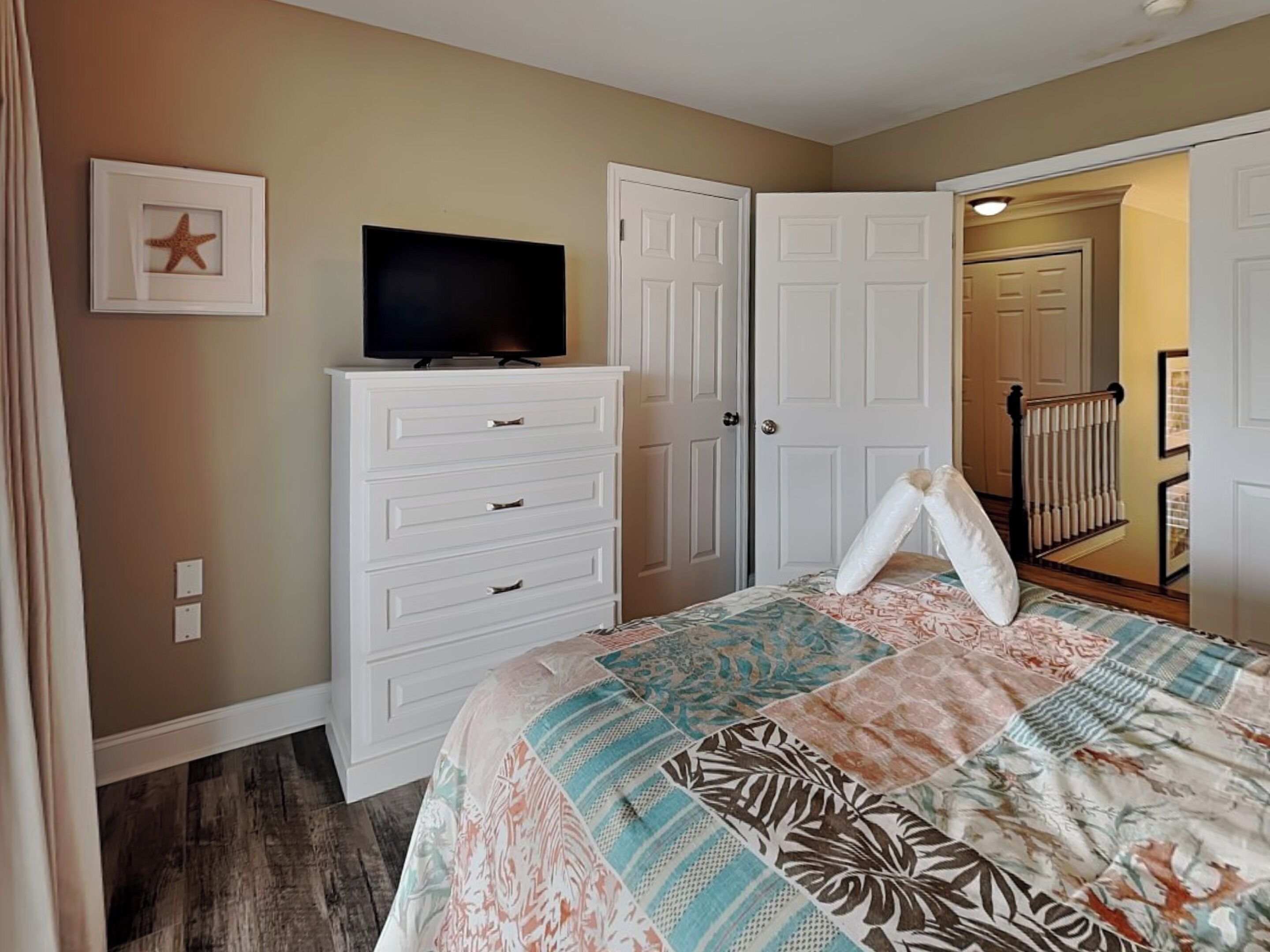 A bedroom with a bed, a dresser, a television, and a door leading to another room.