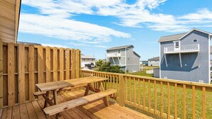 Een houten terras met een picknicktafel, omringd door een houten omheining en huizen op de achtergrond.