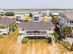 A beachfront property with multiple houses, a covered porch, and a sandy lawn. - Catch A Wave by Topsail Realty (Holly Ridge)