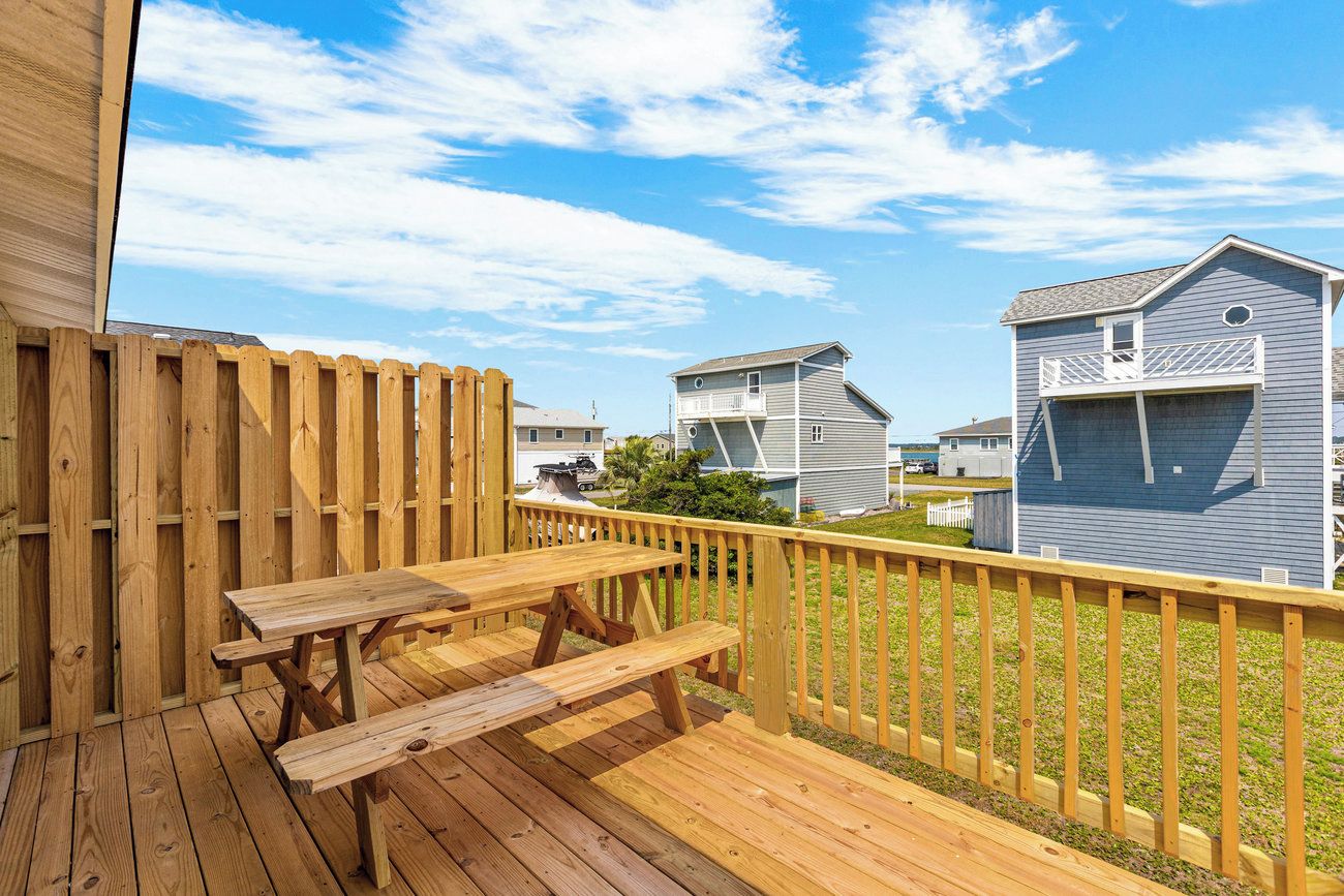 A wooden deck with a picnic table, surrounded by a wooden fence and houses in the background.