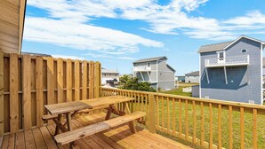 Um deck de madeira com uma mesa de piquenique, cercado por uma cerca de madeira e casas ao fundo.