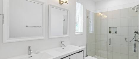 Un baño moderno con dos lavamanos, un inodoro y una ducha con mampara de vidrio.