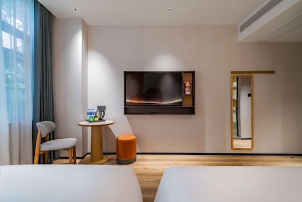 Ein Hotelzimmer mit zwei Betten, einem Fernseher, einem kleinen Tisch mit Stuhl, einem Spiegel und Blick auf die Stadt.
