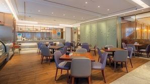 A modern restaurant with wooden flooring, multiple dining tables and chairs, a counter with a menu display, and a glass wall with decorative panels. - Brook Hotel (Hangzhou)