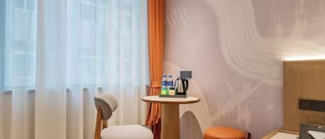 Une chambre d’hôtel avec une chaise en bois, une petite table ronde sur laquelle sont posés des articles de toilette, une lampe fixée au mur et une vue à travers des rideaux transparents.