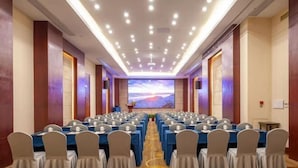A conference room with rows of tables and chairs, a large screen at the front, and a carpeted floor. - Brook Hotel (Hangzhou)
