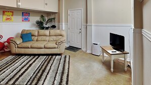 A living room with a beige sofa, a striped rug, a television on a wooden table, and a ceiling fan. - Lucky Ducky by Carolina Retreats (Carolina Beach)