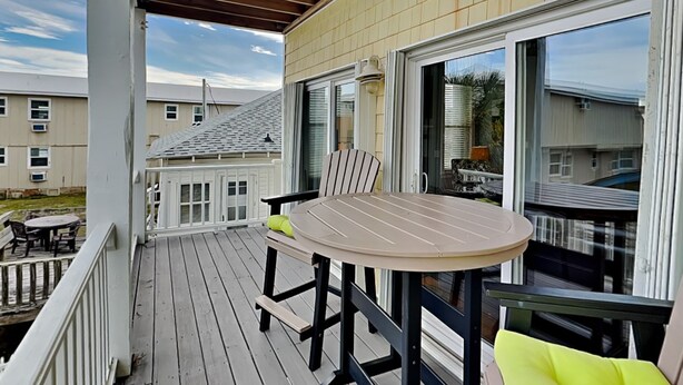 A covered outdoor deck with a round table and chairs, a sliding glass door, and a view of neighboring houses. - Lucky Ducky by Carolina Retreats (Carolina Beach)
