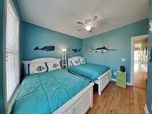 A room with two beds, a ceiling fan, and wall decorations of fish. - Lucky Ducky by Carolina Retreats (Carolina Beach)