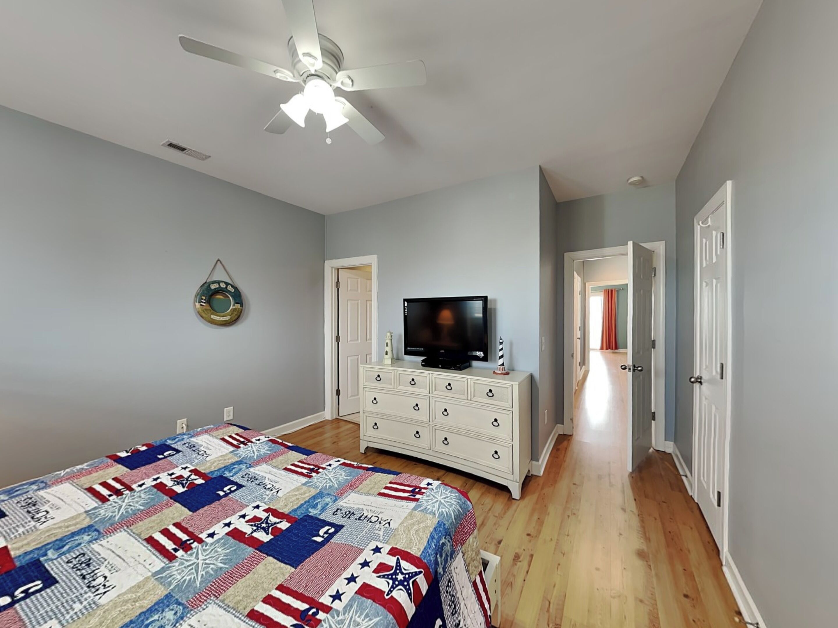 A bedroom with a bed, a television on a dresser, a ceiling fan, and a hallway.