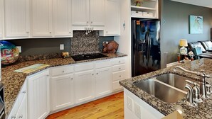 A modern kitchen with white cabinets, granite countertops, a stainless steel refrigerator, and a built-in oven. - Lucky Ducky by Carolina Retreats (Carolina Beach)