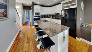 A modern kitchen with a granite countertop, stainless steel appliances, and a bar area with stools. - Lucky Ducky by Carolina Retreats (Carolina Beach)