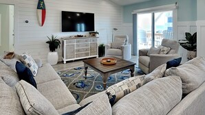 Un salon comprenant un grand canapé, une table basse, un téléviseur fixé au mur et une porte-fenêtre coulissante donnant sur un espace extérieur.