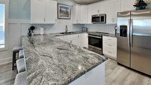 Une cuisine moderne avec des meubles blancs, un plan de travail en granit, des appareils en acier inoxydable et un petit îlot central doté de tabourets de bar.