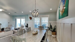 Un coin repas avec une table en bois, des chaises blanches et un lustre.