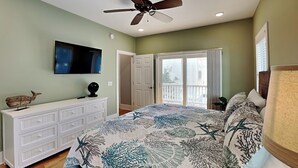 A bedroom with a bed, ceiling fan, TV, dresser, and a door leading to a balcony. - Beaches Be Crazy by Carolina Retreats (Carolina Beach)