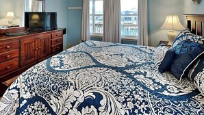 Une chambre à coucher avec un grand lit, une commode, un téléviseur et une fenêtre avec des rideaux.