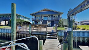 A dock leading to a building with a balcony, a wooden walkway, and a boat. - On Island Time by Topsail Realty (Holly Ridge)