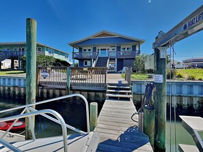 A dock leading to a building with a balcony, a wooden walkway, and a boat. - On Island Time by Topsail Realty (Holly Ridge)