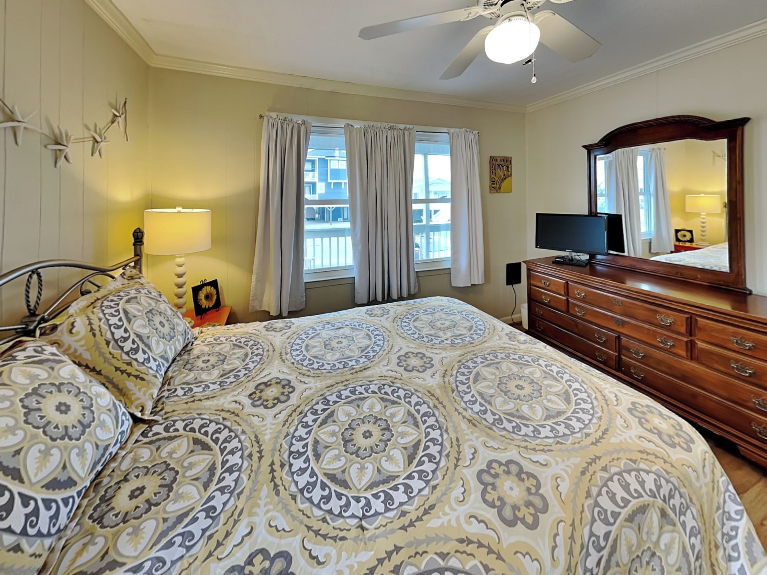 A bedroom with a bed, a dresser, a television, and a window with curtains.