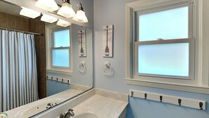 Une salle de bain avec un grand miroir, une baignoire, un lavabo et une fenêtre.