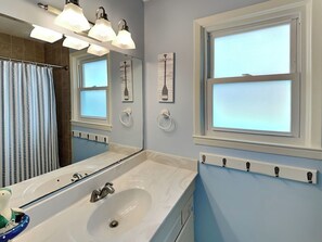 A bathroom with a large mirror, a bathtub, a sink, and a window. - On Island Time by Topsail Realty (Holly Ridge)