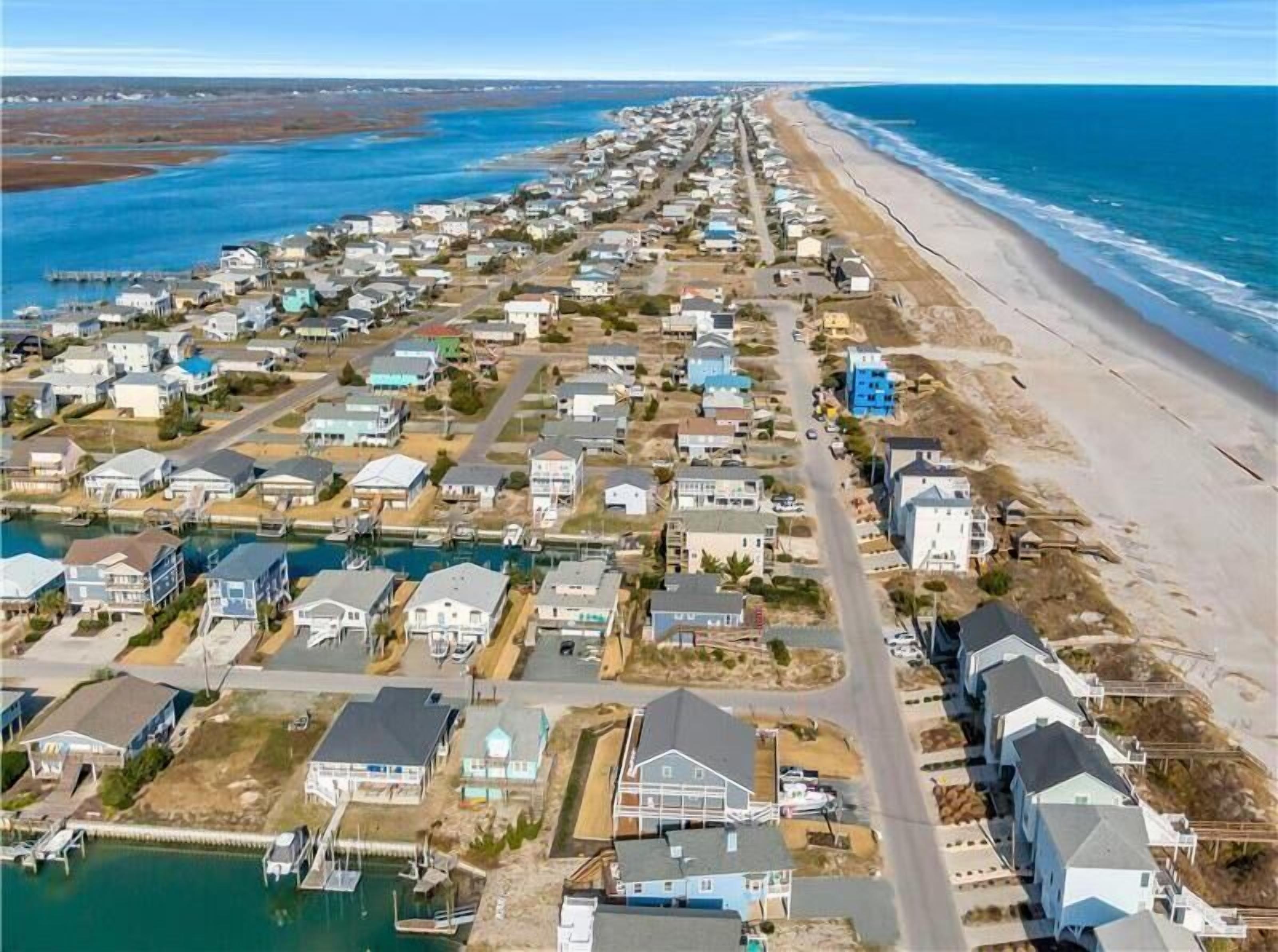 A coastal residential area with houses aligned along the beach, a marina, and a clear view of the ocean.