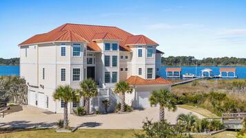 A multi-story house with a red roof, located near a body of water.