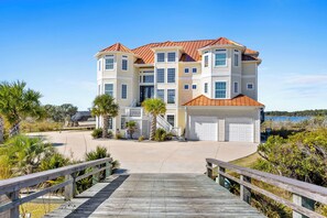 A large, multi-story house with a red roof, a covered porch, and a driveway leading to a wooden dock. - Permuda Private Island by Topsail Realty (Sneads Ferry)
