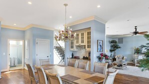 A spacious dining area with a large wooden table and matching chairs, a chandelier, and a staircase leading to a kitchen. - Permuda Private Island by Topsail Realty (Sneads Ferry)